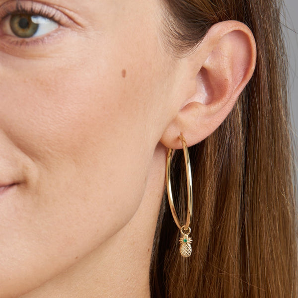 A two piece 14 karat gold hoop earring featuring the pineapple charm with a handset emerald stone. Take off the charm and wear the essential hoops on its own.   The hoop earrings with its very light design are comfortable to wear all day and all night! 